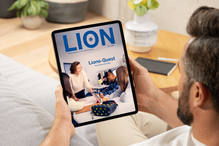 Die aktuelle Ausgabe des Mitgliedermagazins LION wird auf einem Tablet angezeigt. Das Cover zeigt eine Klassenzimmer-Situation: Eine Lehrerin im Gespräch mit Schülern.
