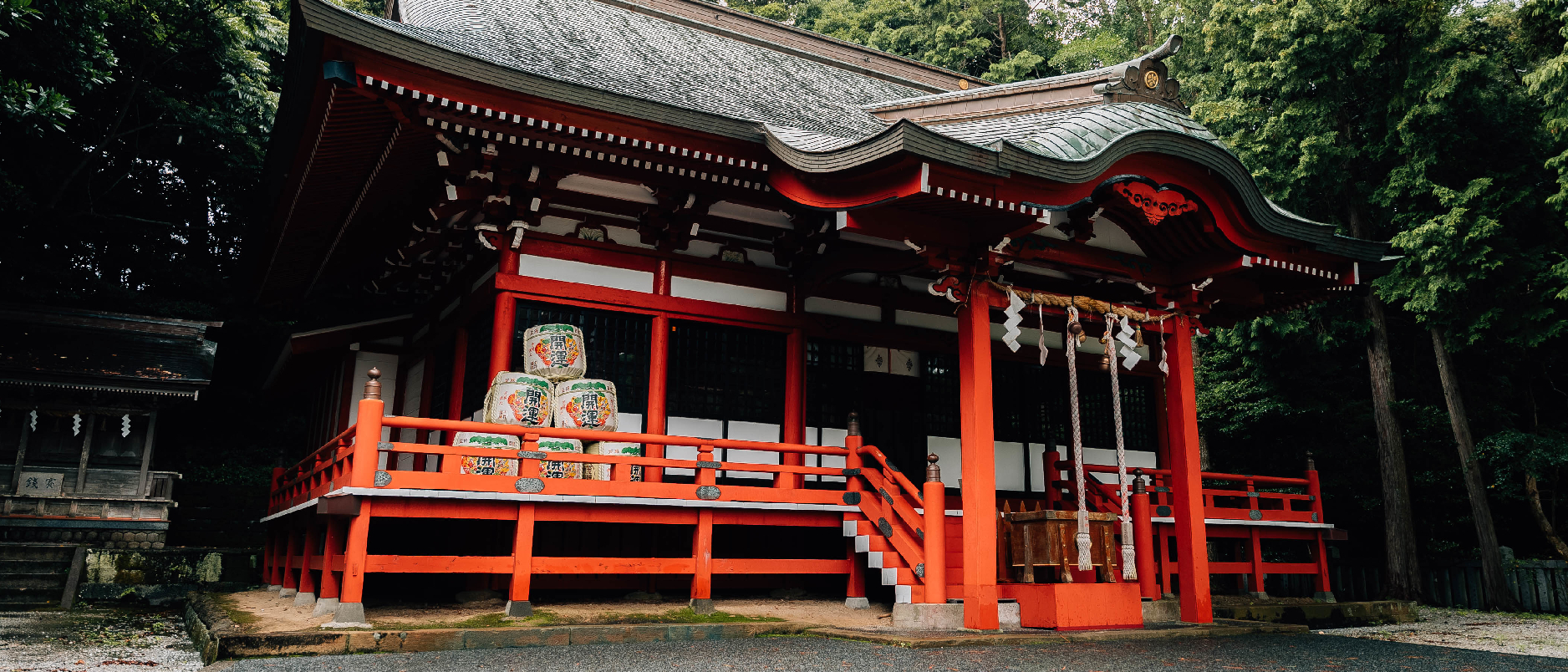 Traditionelles, japanisches Gebäude in rot vor einem grünen Waldhintergrund.