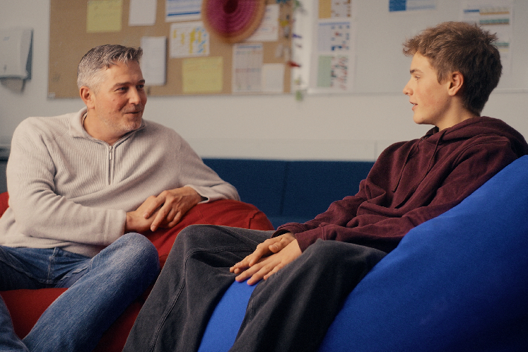 Lehrer und Schüler sitzen in entspannter Atmosphäre auf Sitzsäcken und unterhalten sich